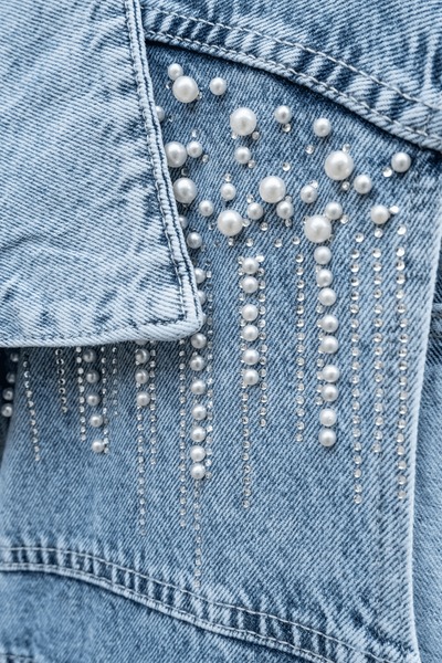 Close-up of white pearls attached beside the collar of a blue denim jacket